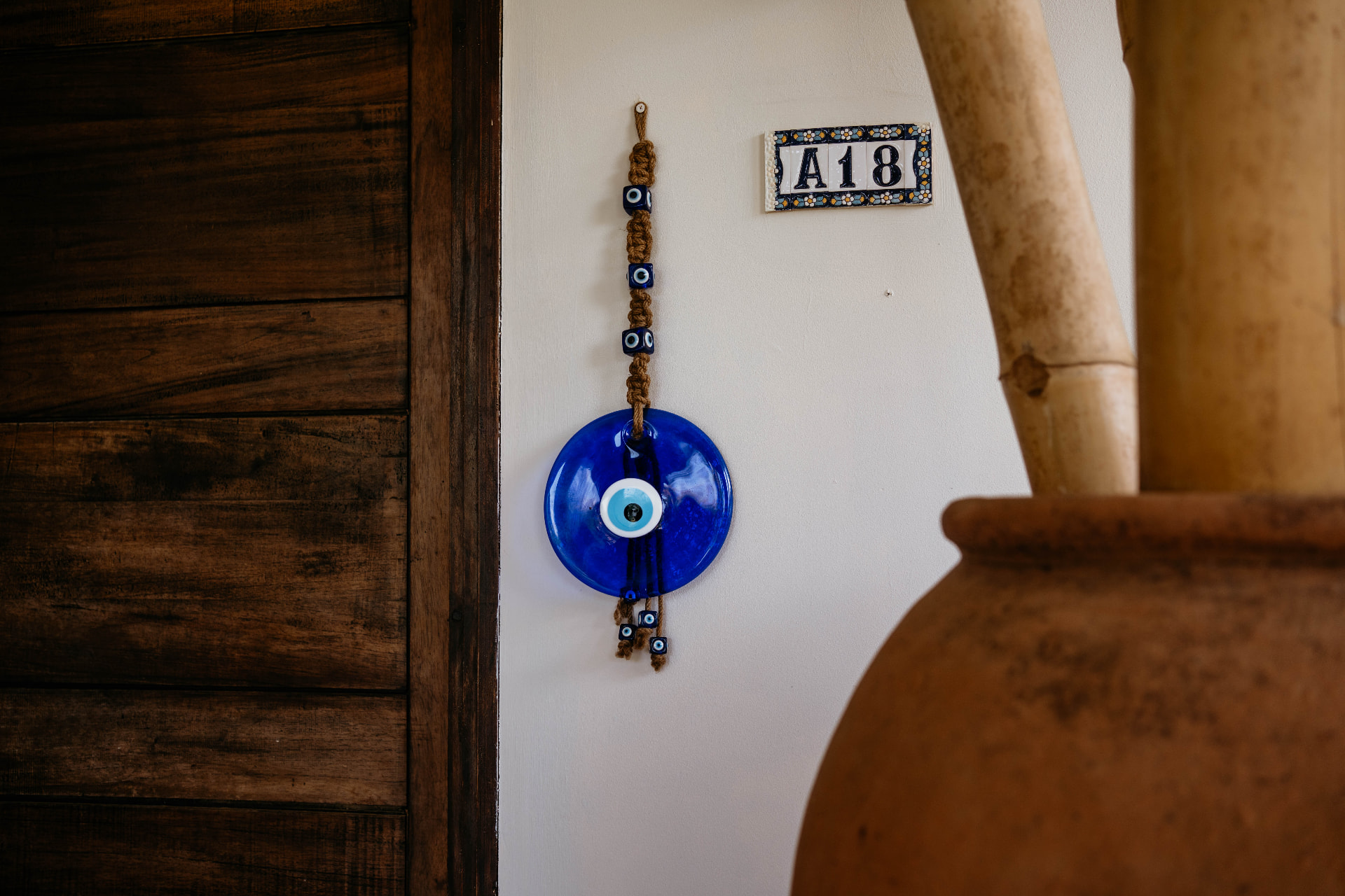 Apartment A18 — entrance with the A18 tile, blue glass eye and terracotta pot