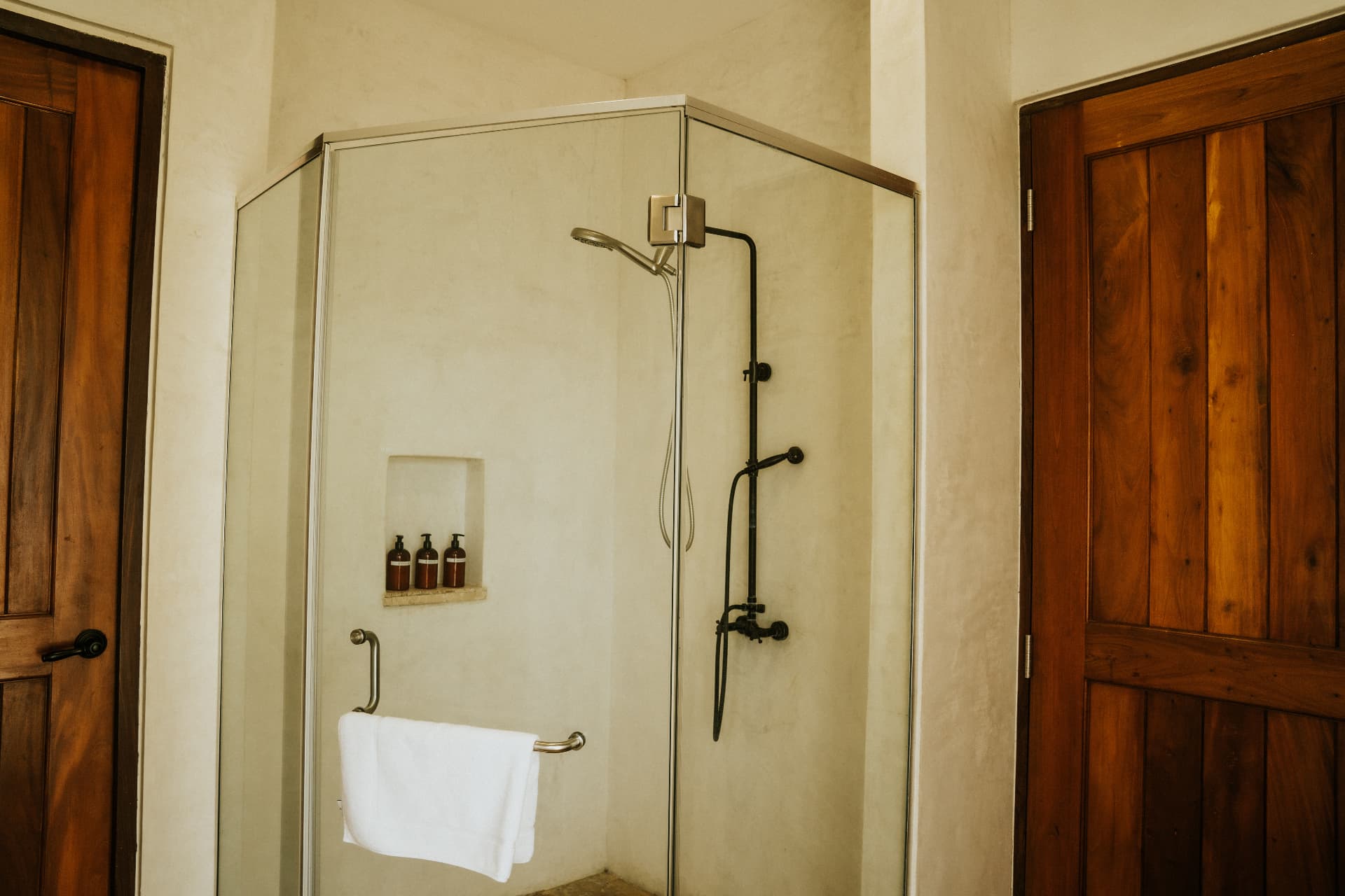 Villa Nomada — en-suite glass shower with plaster walls and teak doors
